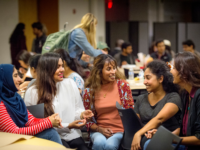 A group of female students sitting and smiling together at fall harvest fest